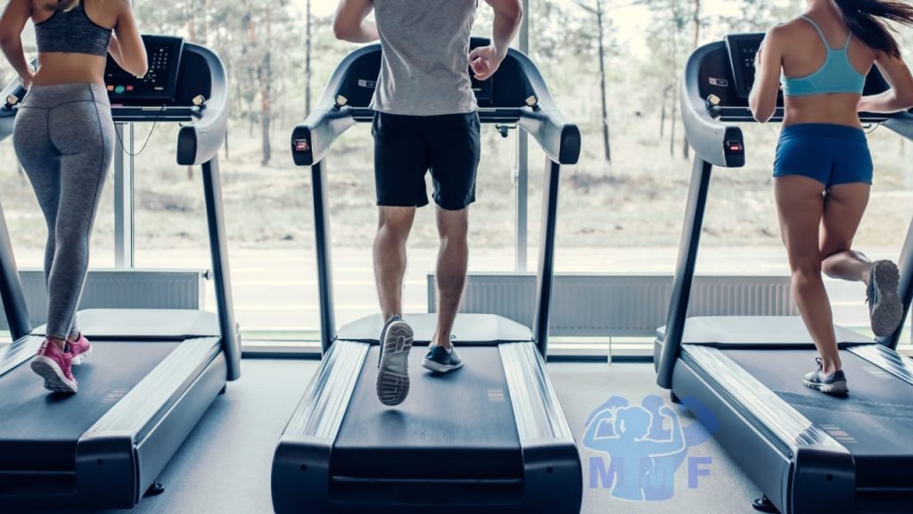 Three fit people running on treadmills looking out a window. Two fit women surrounding one fit man.