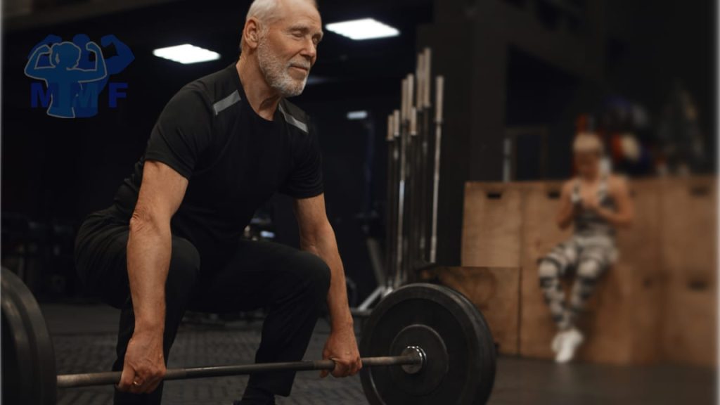 Man in 60s doing deadlifts and build muscle after 50. With a woman in the background looking at her phone.