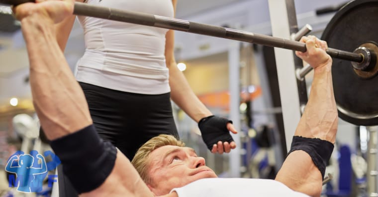 Man performing upper chest exercise incline bench press with a fit woman as his spotter.