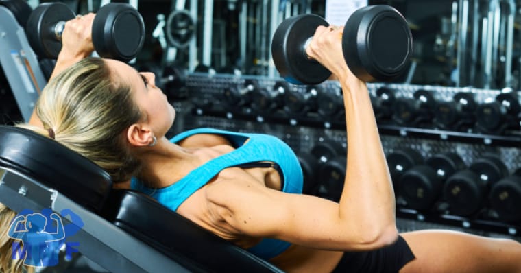 Fit woman performing upper chest exercise incline dumbbell press.